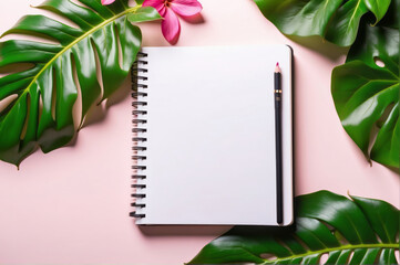 blank notebook lies open on a pink surface, framed by lush green tropical leaves, top view