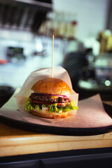 Burger with cheese on wax paper on plastic tray on wooden table. Fresh tasty burger on dark...