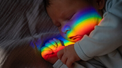 Close-up portrait of a newborn boy with a prism beam on his face. Rainbow.