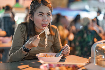 Traveler Asian woman enjoy eating noodle at night market. traditional Chiang Mai Thailand street food.