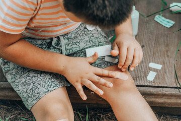 Close-up of a child's leg injury. The child injured his knee. A boy puts a Band-Aid on a wound...
