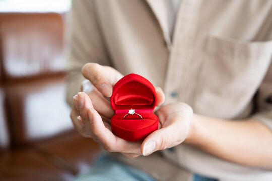 Wedding proposal surprise gift with luxury diamond ring in red heart jewellery box while groom hand holding and open it. Prepare for bridal engagement culture in Valentine day