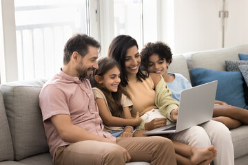 Happy Latin parents and two kids enjoying online entertainment with laptop, using Internet technology, application, communication, looking at computer screen together, laughing