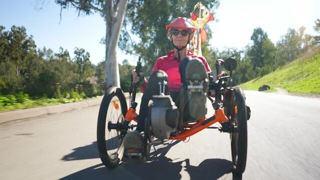 Closeup low angle of elderly senior woman riding recumbent tricycle e-bike on a path on a sunny day in a park.