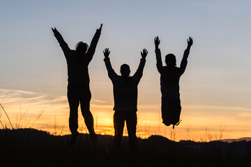 Silhouette happy three people jumping on mountain sunset sky background.