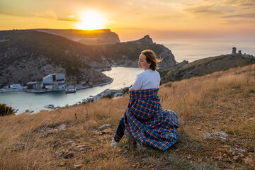 Happy woman on sunset in mountains. Woman siting with her back on the sunset in nature in summer....