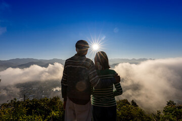Back view of senior couple watching sunrise together with panoramic misty mountain view after...