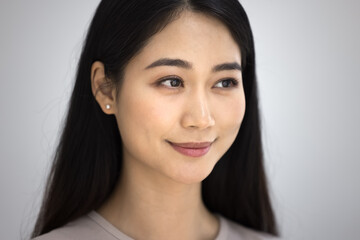 Positive beautiful young Asian woman close up casual portrait. Happy Korean girl, beauty care model with perfect skin and natural makeup looking away with pensive smile