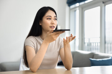 Serious young adult Chinese smartphone user girl talking on speaker, speaking at mobile phone,...