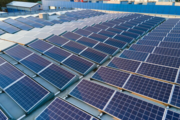 Aerial view of solar power plant with blue photovoltaic panels mounted on industrial building roof...
