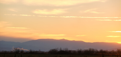 Beautiful evening panoramic landscape with bright setting sun over distant mountain peaks at sunset