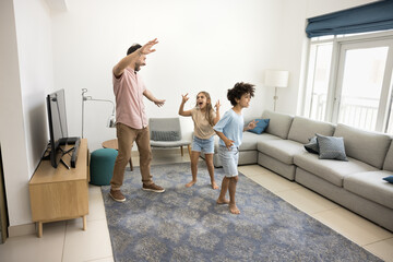 Happy cheerful dad and excited sibling kids having fun at home, dancing and singing to rock music, shouting in living room, enjoying family entertainment, leisure, childhood