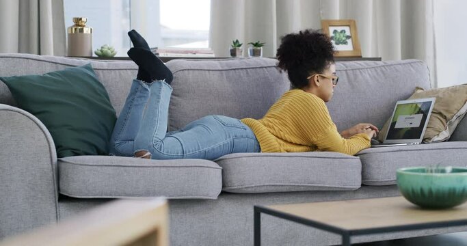 Woman, typing and laptop on couch with relax for online search, social media and technology in living room. Young person, wellness and work on computer, glasses and digital or reading ebook on sofa