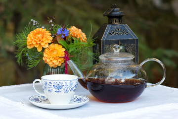 Patio table with cup of tea, pot, flowers and lantern.