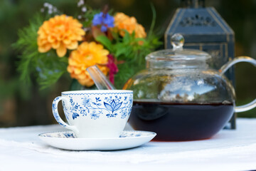 Patio table with cup of tea, pot, flowers and lantern.