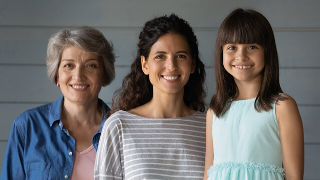 Mothers and daughters. Happy intergenerational latin family of 3 diverse age females pose for portrait together. Cute little girl look at camera smile standing with millennial mom and old age grandma - Powered by Adobe