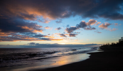 A sunset on Waimea Beach on Kauai reflects warmth onto gentle waves and a glow on the dark sand.