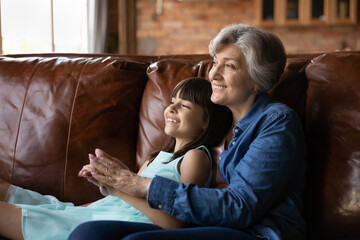Visiting granny. Happy little preteen latina girl relax on couch in embraces of beloved...