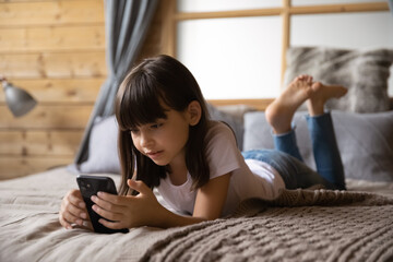 Internet addiction and safety. Curious preteen girl stay at home alone lie on bed surf websites on smartphone online read blogs watch web video channels. School age child relax browsing social media - obrazy, fototapety, plakaty