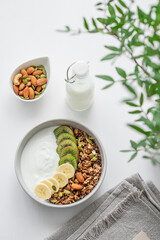 Granola with banana and kiwi on a white table with a green branch.