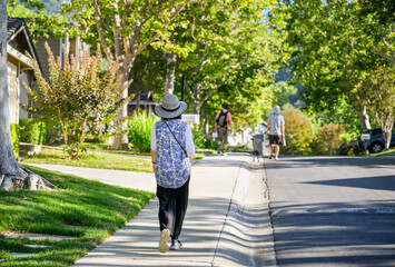 Three people walking on the pedestrian footpath in a leafy suburb. California.