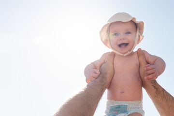 Baby held high against a sunny backdrop by a loving father. Concept of joy and freedom in early childhood