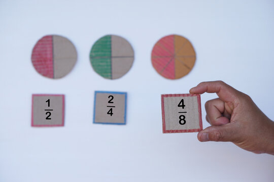Hand hold paper card with fraction numbers. Circle paper show parts of color separation. Concept, Math teaching. Education. DIY craft as teaching aid in Math subject.            