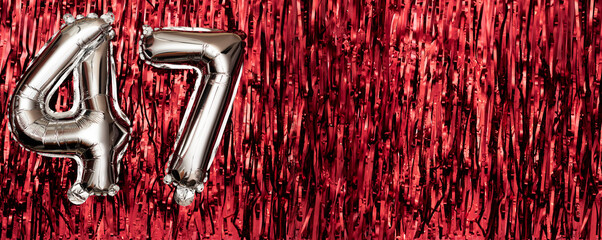 Silver foil balloon number 47 on a background of red tinsel decoration. Birthday greeting card,...