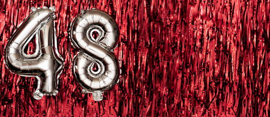 Silver foil balloon number 48 on a background of red tinsel decoration. Birthday greeting card,...