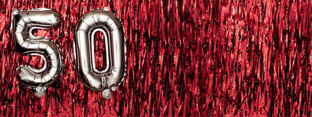 Silver foil balloon number 50 on a background of red tinsel decoration. Birthday greeting card,...