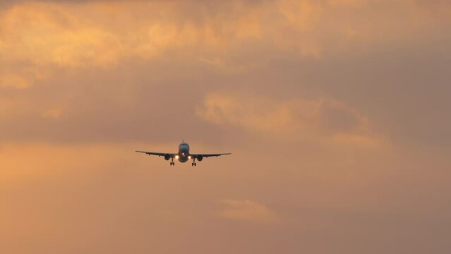 Cinematic shot of a jet plane approaching landing. Passenger airliner flies in the sunset sky, front view, long shot