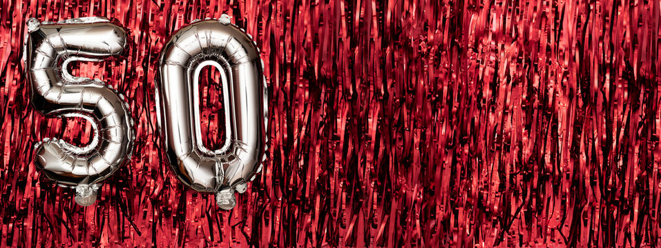 Silver foil balloon number 50 on a background of red tinsel decoration. Birthday greeting card, inscription fifty. Anniversary event. Banner.