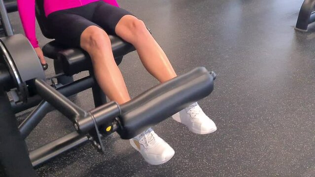 Female legs during training of quadriceps muscles of thigh at strength machine in gym. Training exercises for biceps legs