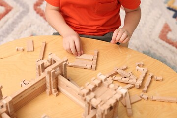 Little boy playing with wooden construction set at table in room, closeup. Child's toy