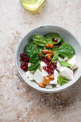Salad with fresh spinach, feta cheese, pomegranate seeds and almonds, vertical shot on a beige granite background, elevated view