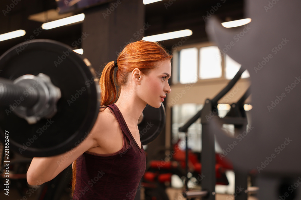 Wall mural Athletic young woman with barbell training in gym