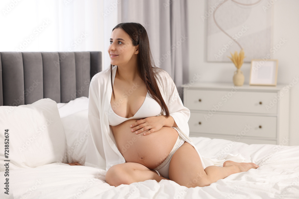 Poster Beautiful pregnant woman in stylish comfortable underwear and robe on bed at home