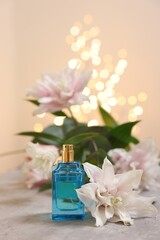 Obraz na płótnie Canvas Bottle of perfume and beautiful lily flowers on table against beige background with blurred lights, closeup