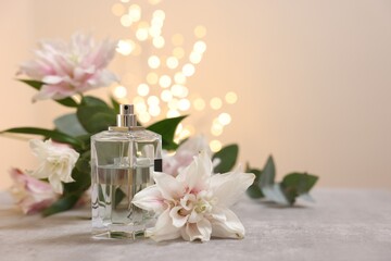 Fototapeta na wymiar Bottle of perfume and beautiful lily flowers on table against beige background with blurred lights, space for text