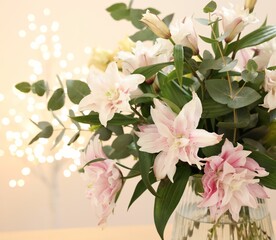 Bouquet of beautiful lily flowers in vase against beige background with blurred lights, closeup