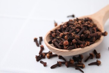 Spoon with aromatic dried clove buds on light table, closeup. Space for text