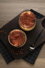 Delicious tiramisu in glasses, spoon and coffee beans on wooden table, top view