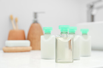 Mini bottles of cosmetic products on white countertop in bathroom. Space for text