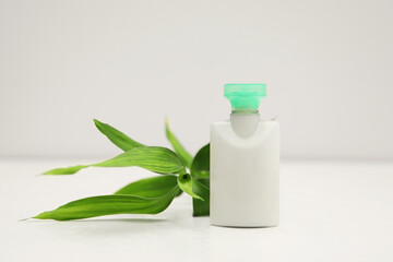 Mini bottle of cosmetic product and green branch on light background