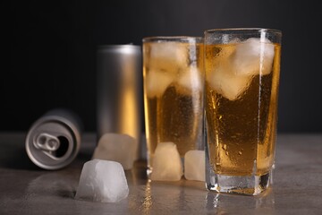 Tasty energy drink with ice cubes in glasses and aluminium cans on grey table, closeup