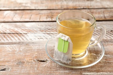 Tea bag in glass cup on wooden table, space for text