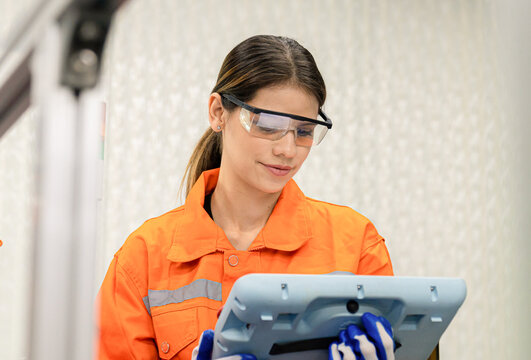Professional Female automation engineer in orange with helmet safety inspection remotely controls industrial robot arm welding machine ,robot arm concept - Powered by Adobe