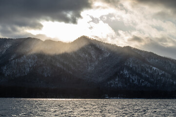 雲に遮られた夕陽の光が山に射す山間の湖のドラマチックな風景。北海道の屈斜路湖。