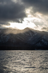 雲に遮られた夕陽の光が山に射す山間の湖のドラマチックな風景。北海道の屈斜路湖。