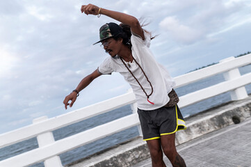 Filipino skateboarder with free spirit joining street sports riding over a bridge at dusk, Philippines